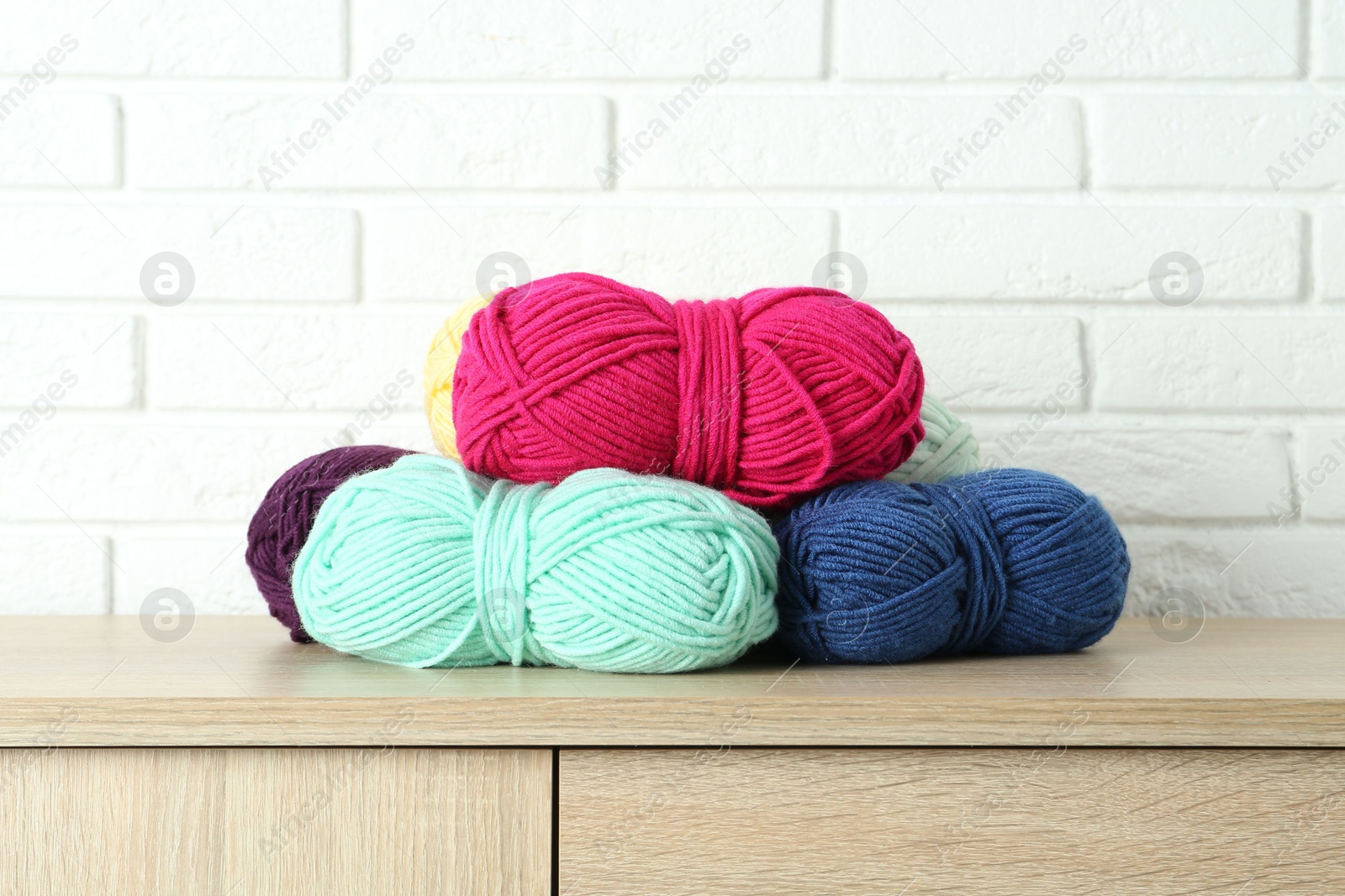 Photo of Skeins of yarn on wooden chest of drawers near white brick wall