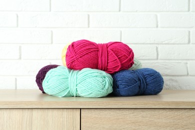 Photo of Skeins of yarn on wooden chest of drawers near white brick wall