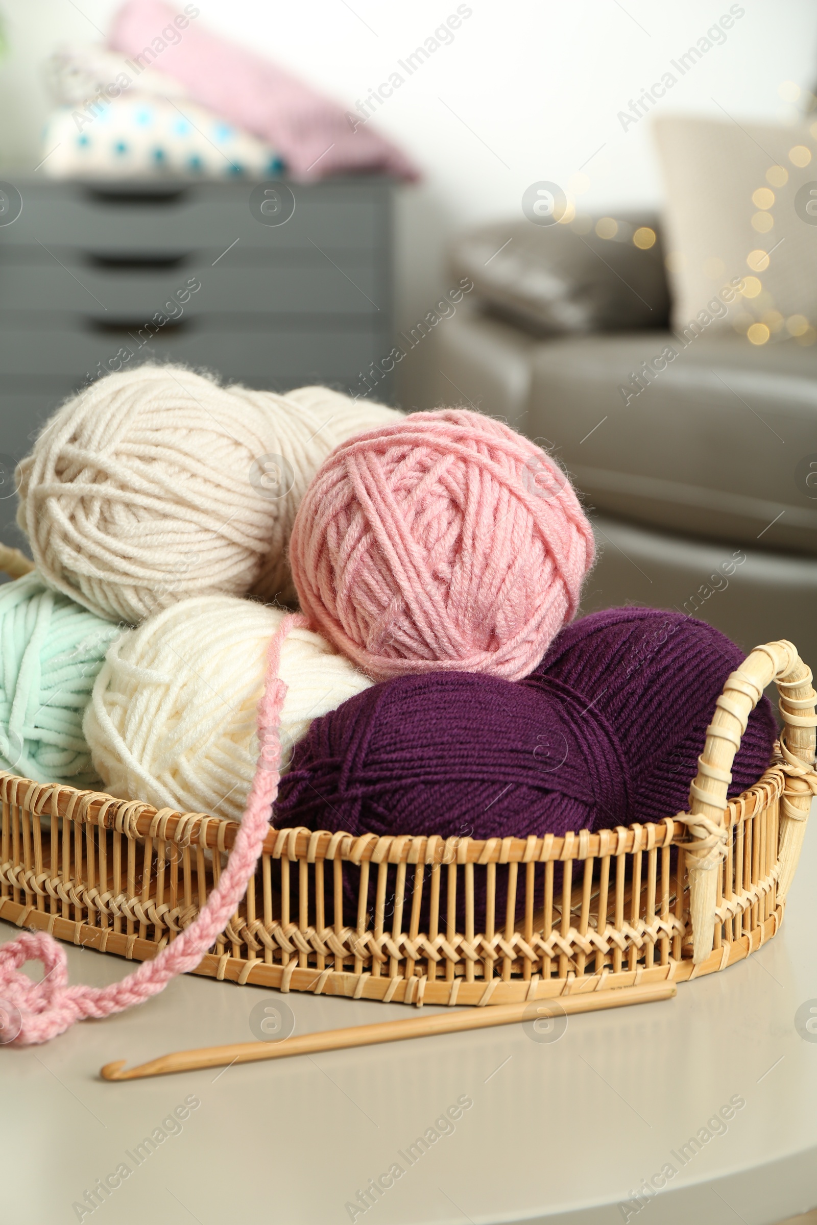 Photo of Wicker basket with colorful yarns, crochet pattern, and hook on table indoors