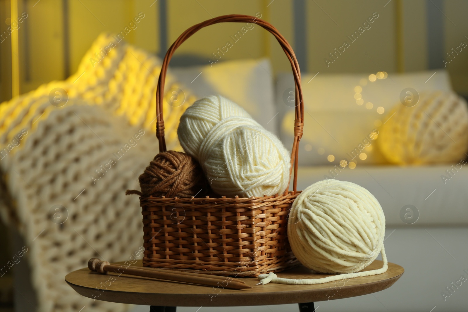 Photo of Wicker basket with colorful yarns and knitting needles on coffee table in cozy room