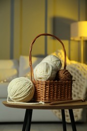 Photo of Wicker basket with colorful yarns and knitting needles on coffee table in cozy room