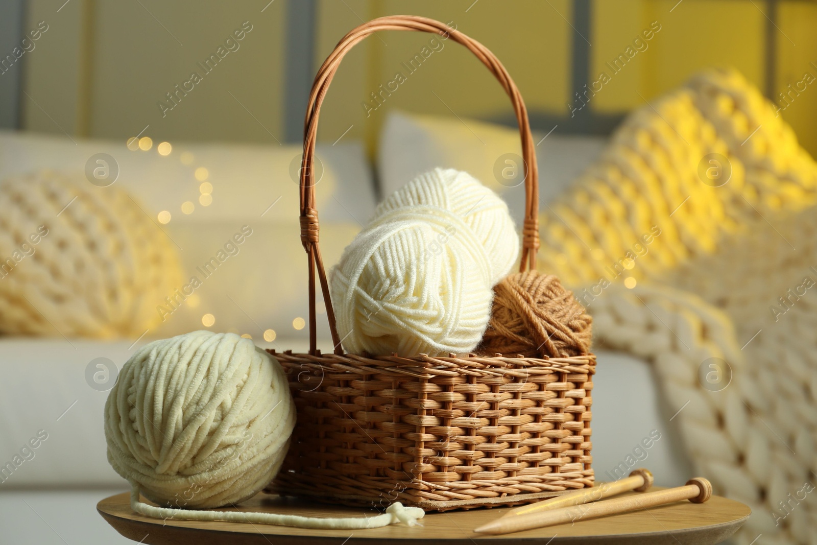 Photo of Wicker basket with colorful yarns and knitting needles on coffee table in cozy room