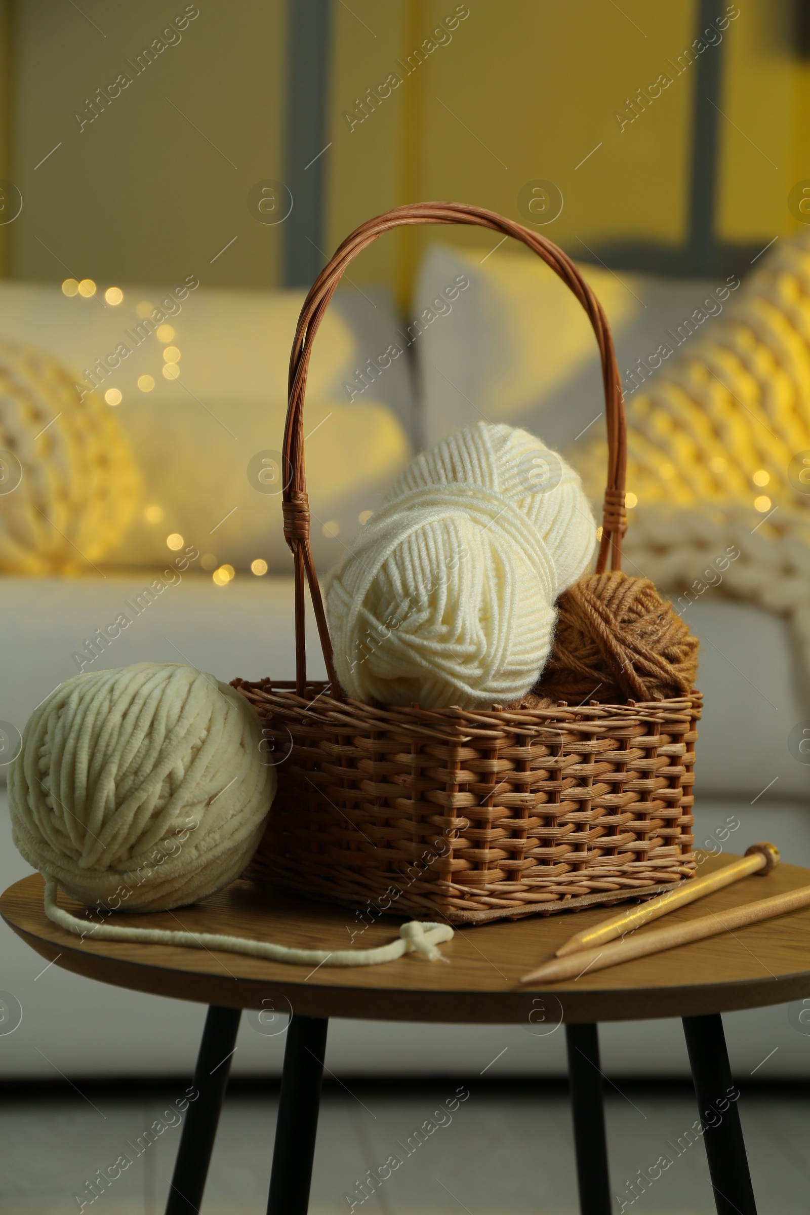 Photo of Wicker basket with colorful yarns and knitting needles on coffee table in cozy room