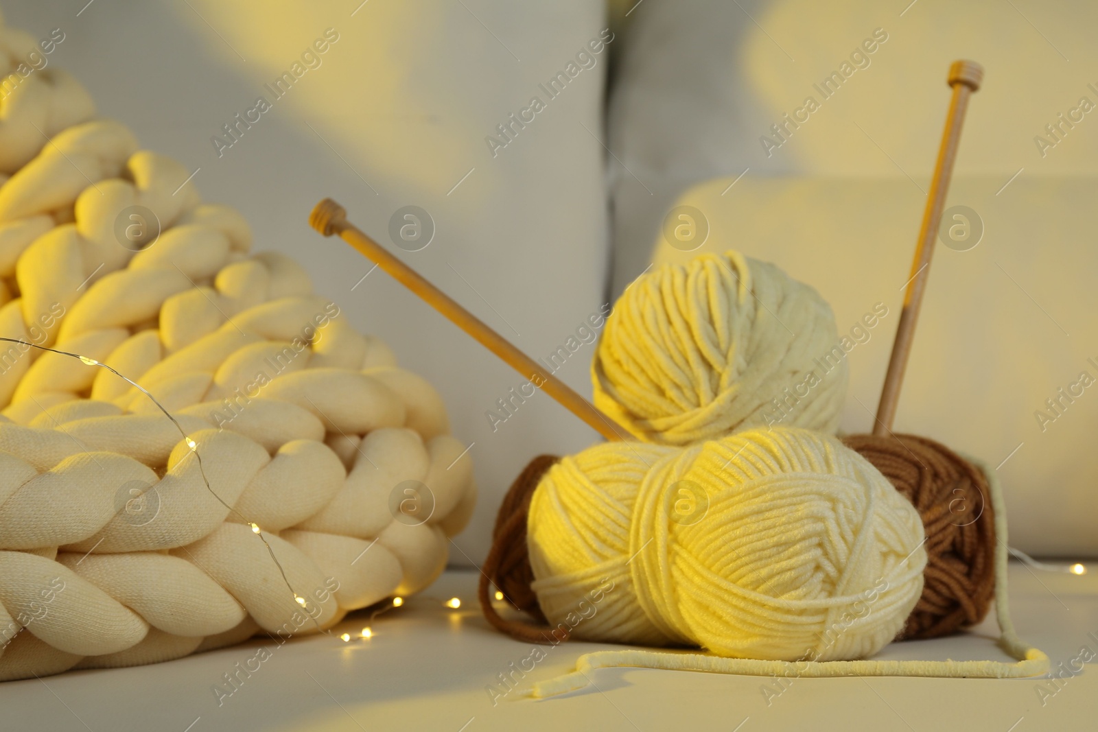 Photo of Skeins of yarn, knitting needles and festive lights on sofa