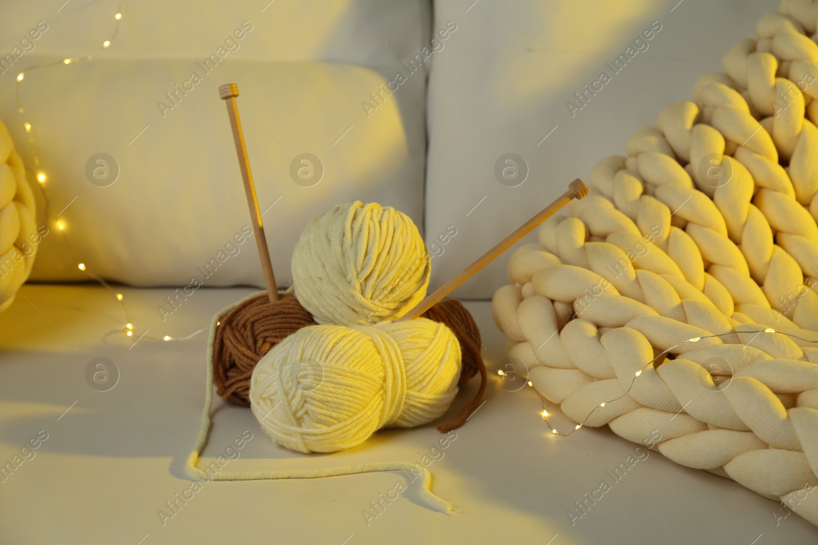 Photo of Skeins of yarn, knitting needles and festive lights on sofa