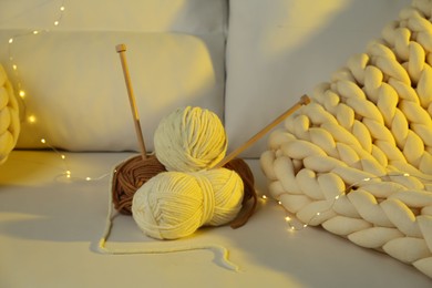 Photo of Skeins of yarn, knitting needles and festive lights on sofa