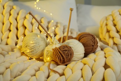 Photo of Colorful yarns, knitting needles and festive lights on blanket