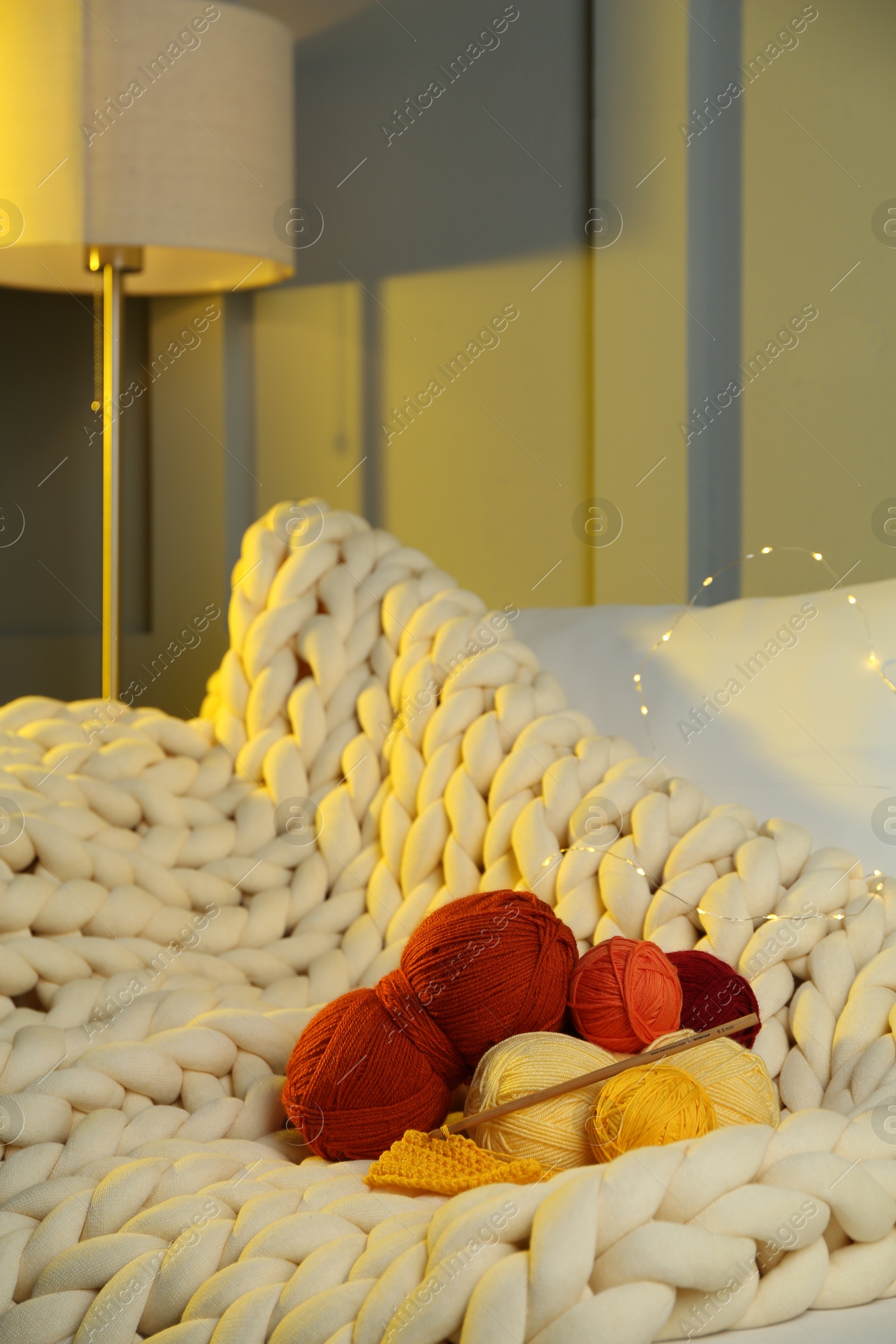 Photo of Colorful yarns, crochet pattern, hook and festive lights on blanket in room