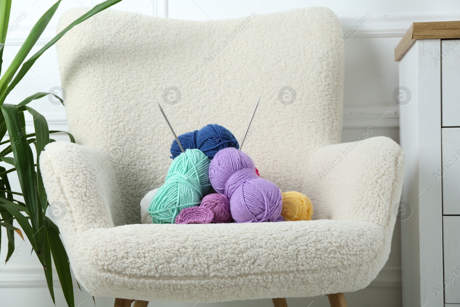 Photo of Pile of colorful yarns, crochet pattern and knitting needles on soft armchair indoors