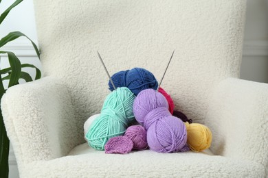 Photo of Pile of colorful yarns, crochet pattern and knitting needles on soft armchair, closeup