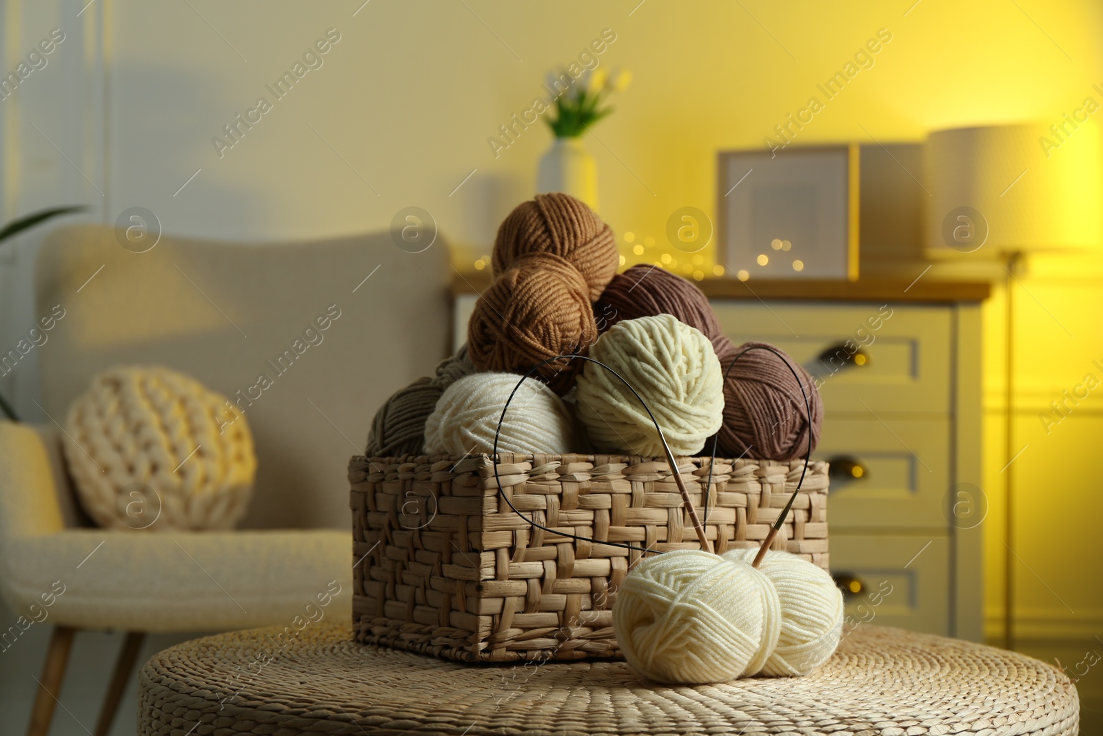 Photo of Wicker basket with colorful yarns and knitting needles on coffee table in cozy room