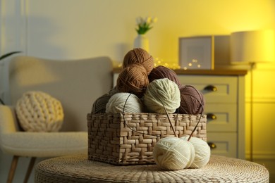 Photo of Wicker basket with colorful yarns and knitting needles on coffee table in cozy room