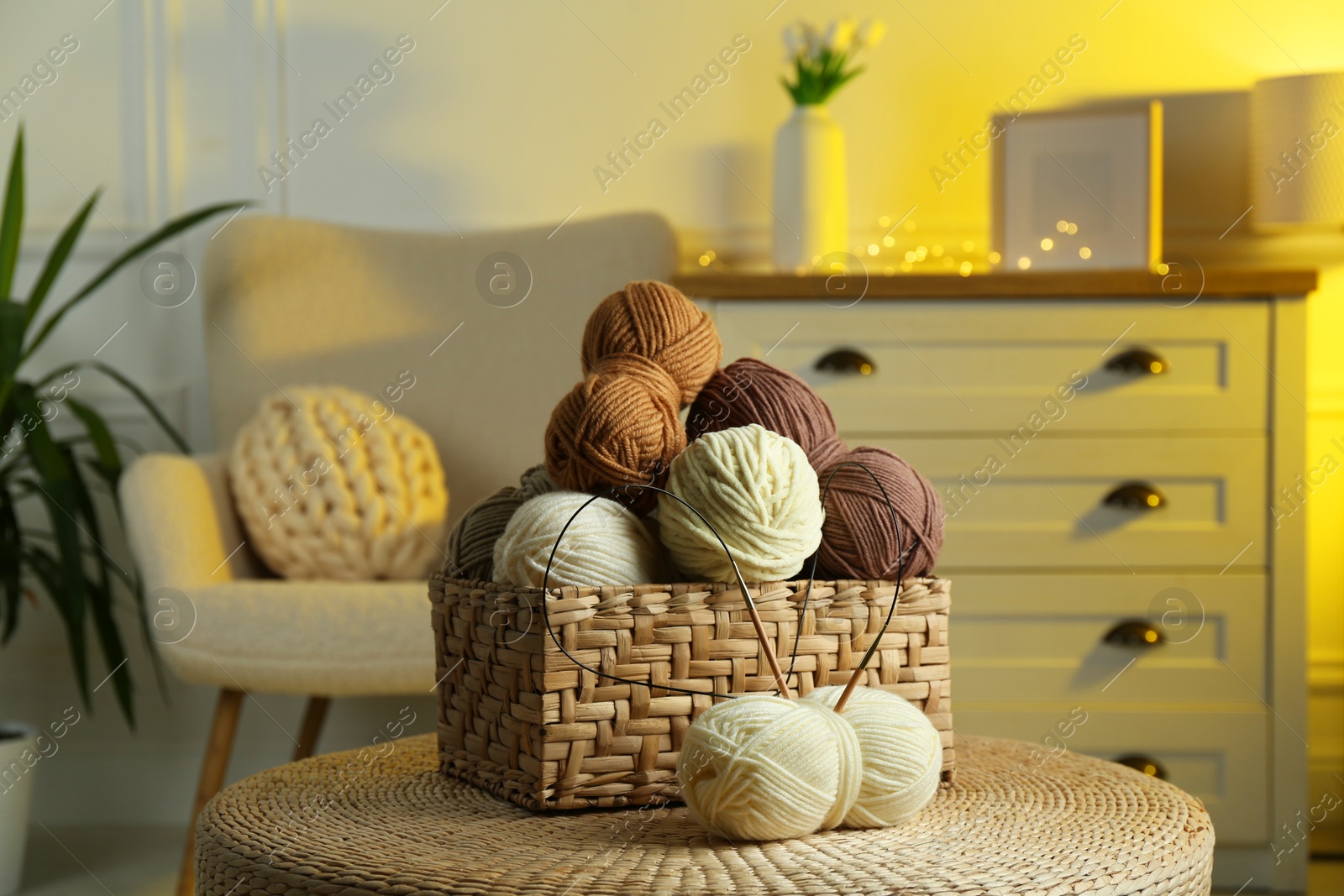 Photo of Wicker basket with colorful yarns and knitting needles on coffee table in cozy room