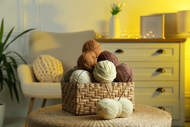 Photo of Wicker basket with colorful yarns and knitting needles on coffee table in cozy room