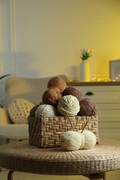 Photo of Wicker basket with colorful yarns and knitting needles on coffee table in cozy room