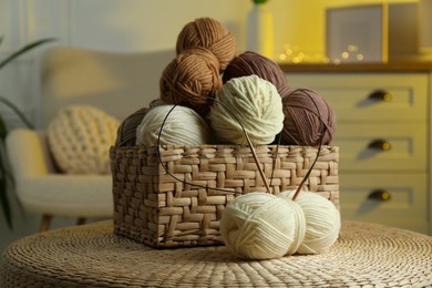 Photo of Wicker basket with colorful yarns and knitting needles on coffee table in cozy room