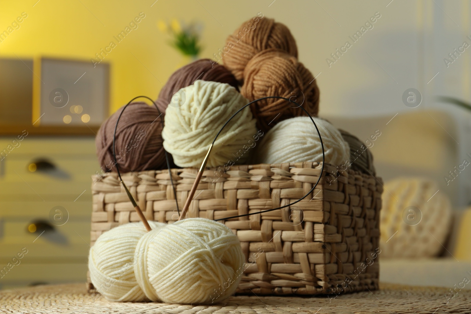 Photo of Wicker basket with colorful yarns and knitting needles in cozy room, closeup