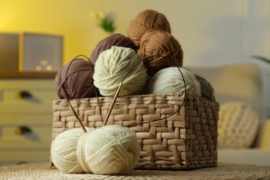 Wicker basket with colorful yarns and knitting needles in cozy room, closeup