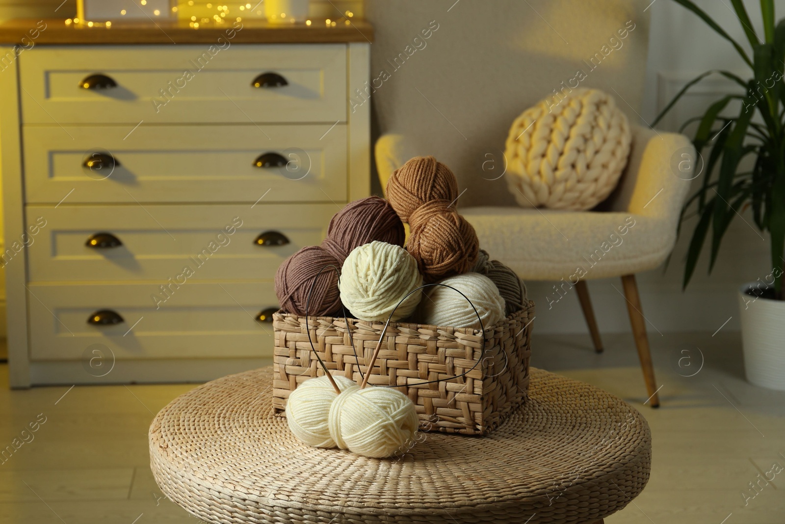 Photo of Wicker basket with colorful yarns and knitting needles on coffee table in cozy room