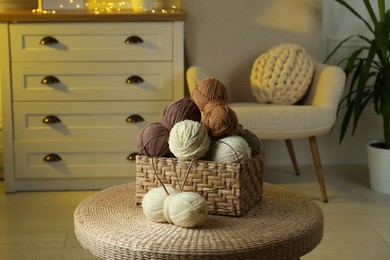 Photo of Wicker basket with colorful yarns and knitting needles on coffee table in cozy room