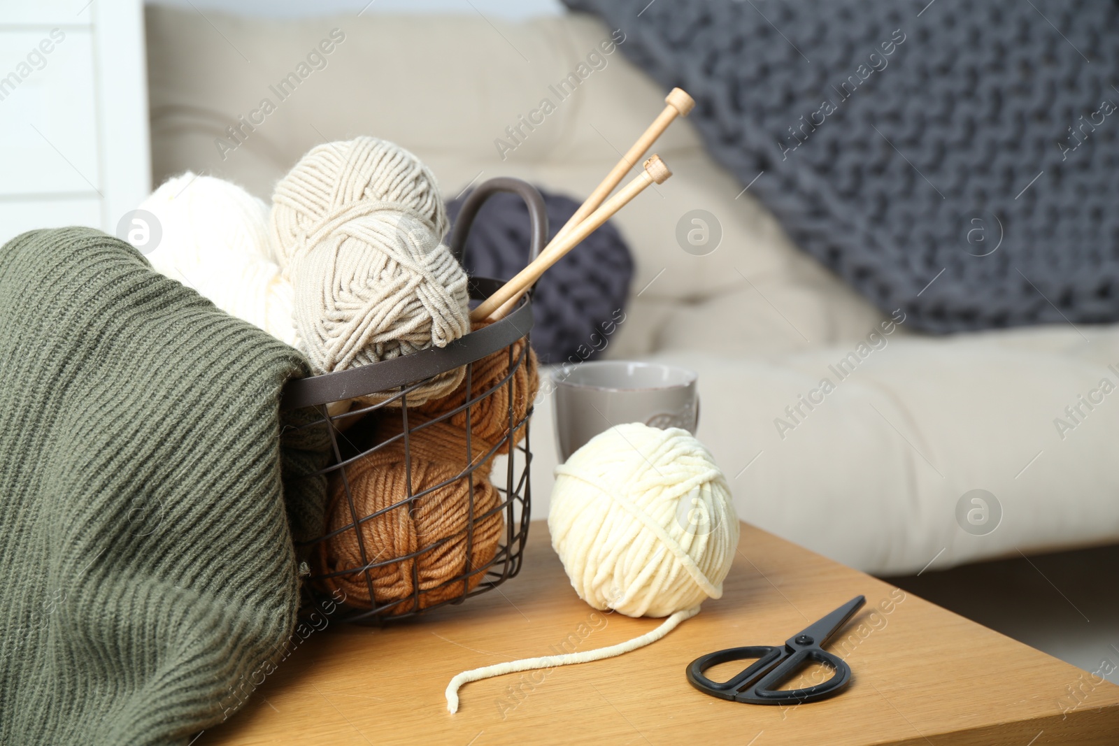 Photo of Basket with yarns, knitting needles, scissors and sweater on wooden table indoors