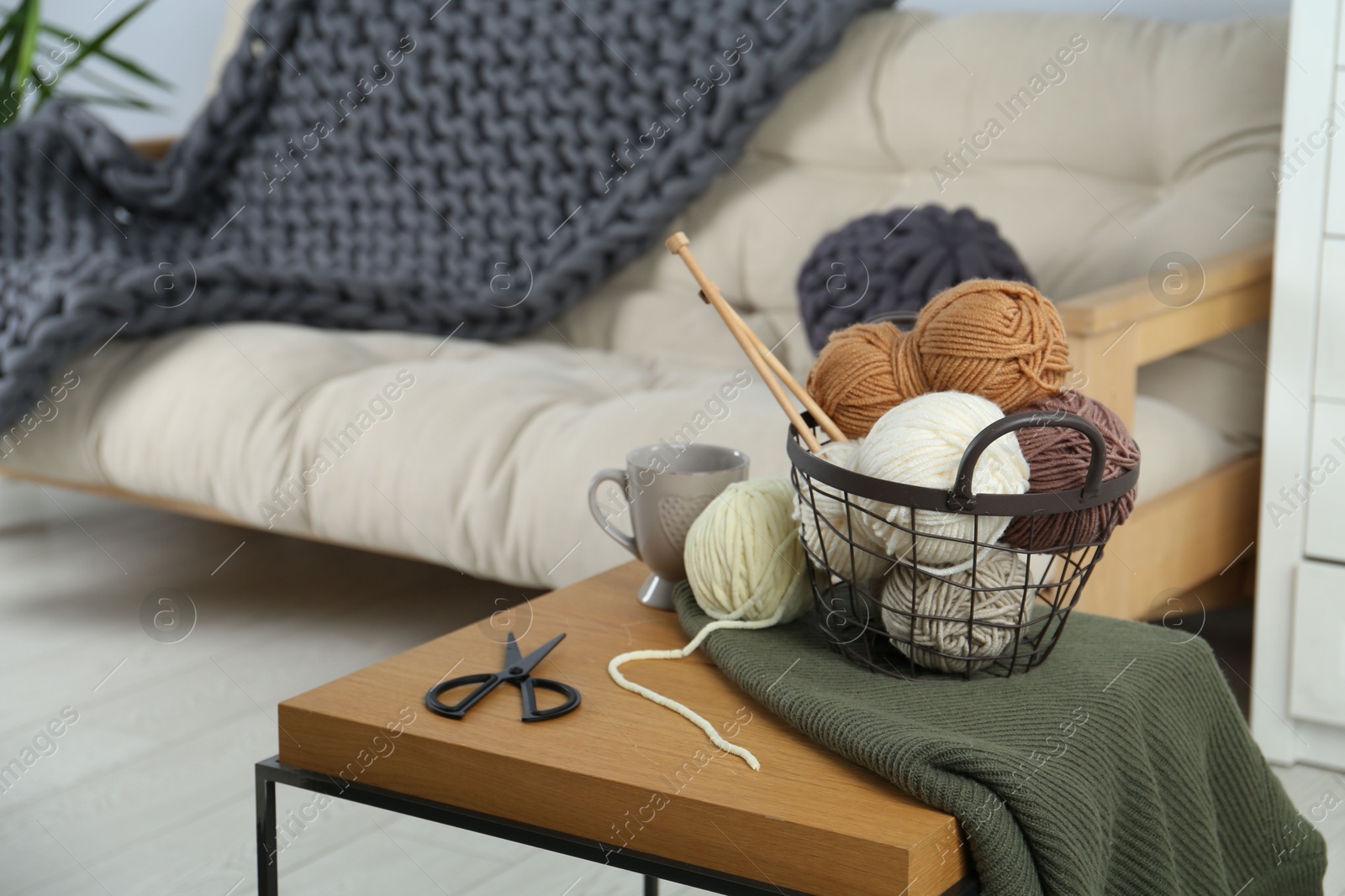 Photo of Basket with yarns, knitting needles, scissors and sweater on coffee table indoors