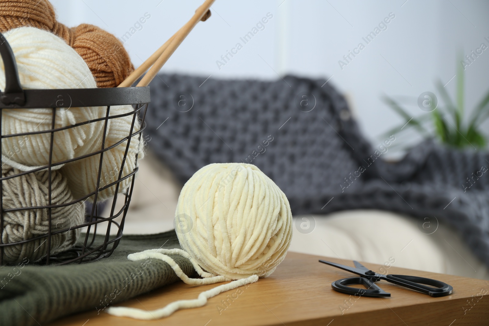 Photo of Basket with yarns, knitting needles, scissors and sweater on wooden table indoors