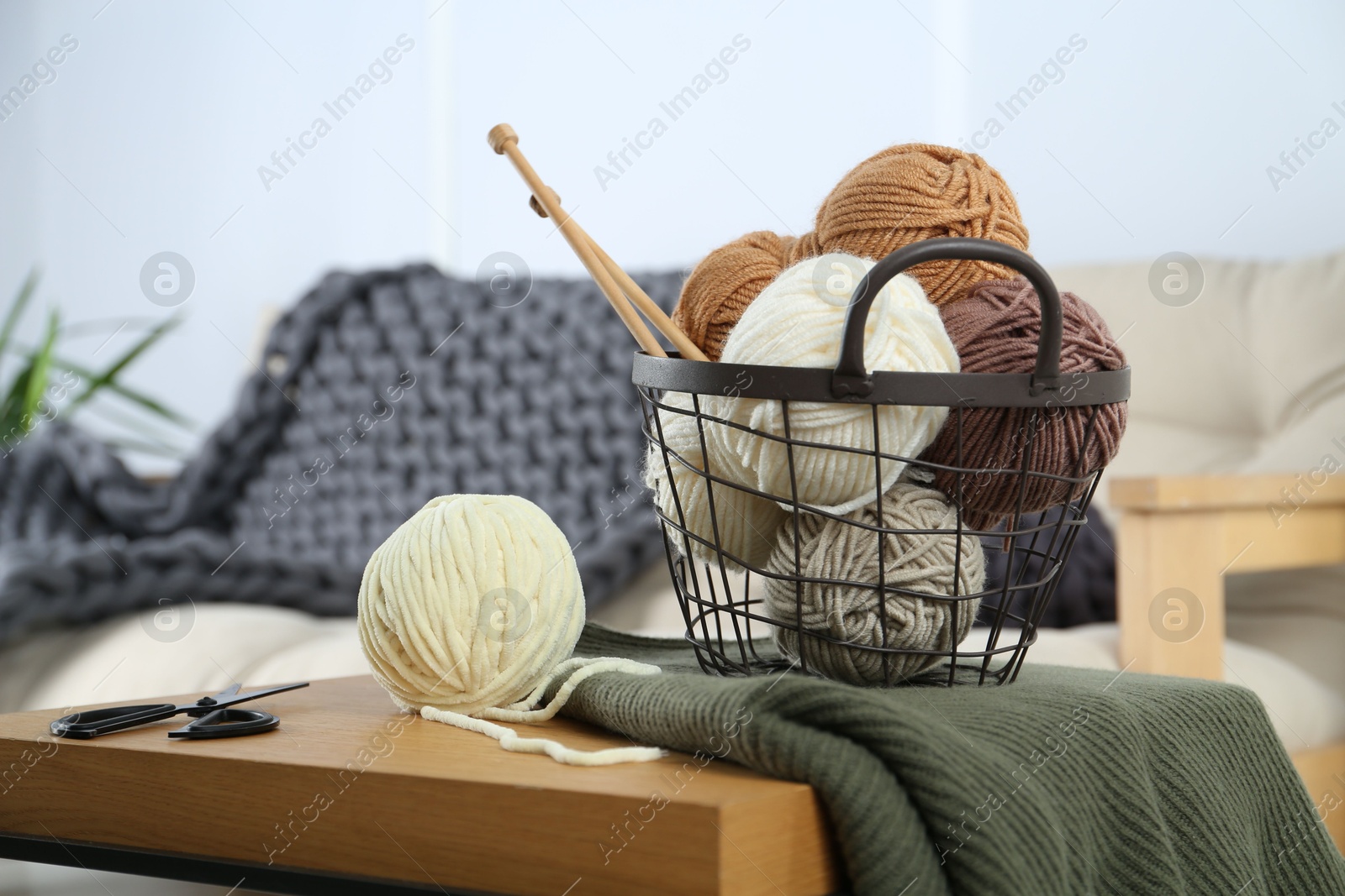 Photo of Basket with yarns, knitting needles, scissors and sweater on wooden table indoors