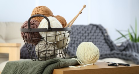 Photo of Basket with yarns, knitting needles, scissors and sweater on wooden table indoors