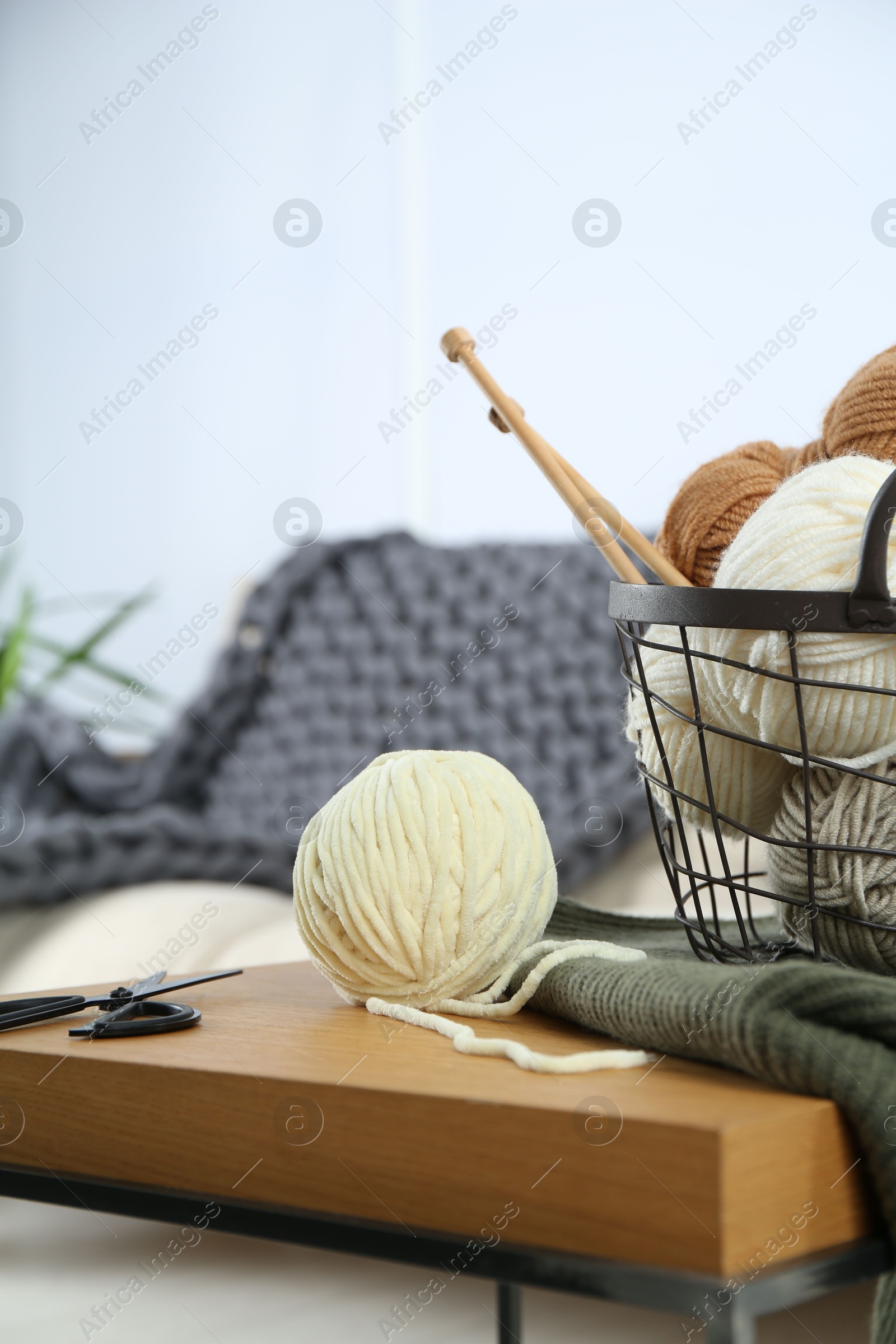 Photo of Basket with yarns, knitting needles, scissors and sweater on wooden table indoors