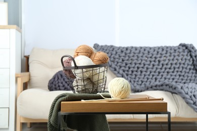 Basket with yarns, knitting needles and sweater on coffee table indoors