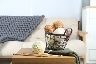 Photo of Basket with yarns, knitting needles and sweater on coffee table indoors