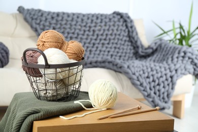 Photo of Basket with yarns, knitting needles and sweater on coffee table indoors