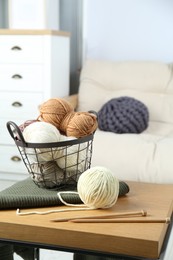 Basket with yarns, knitting needles and sweater on coffee table indoors