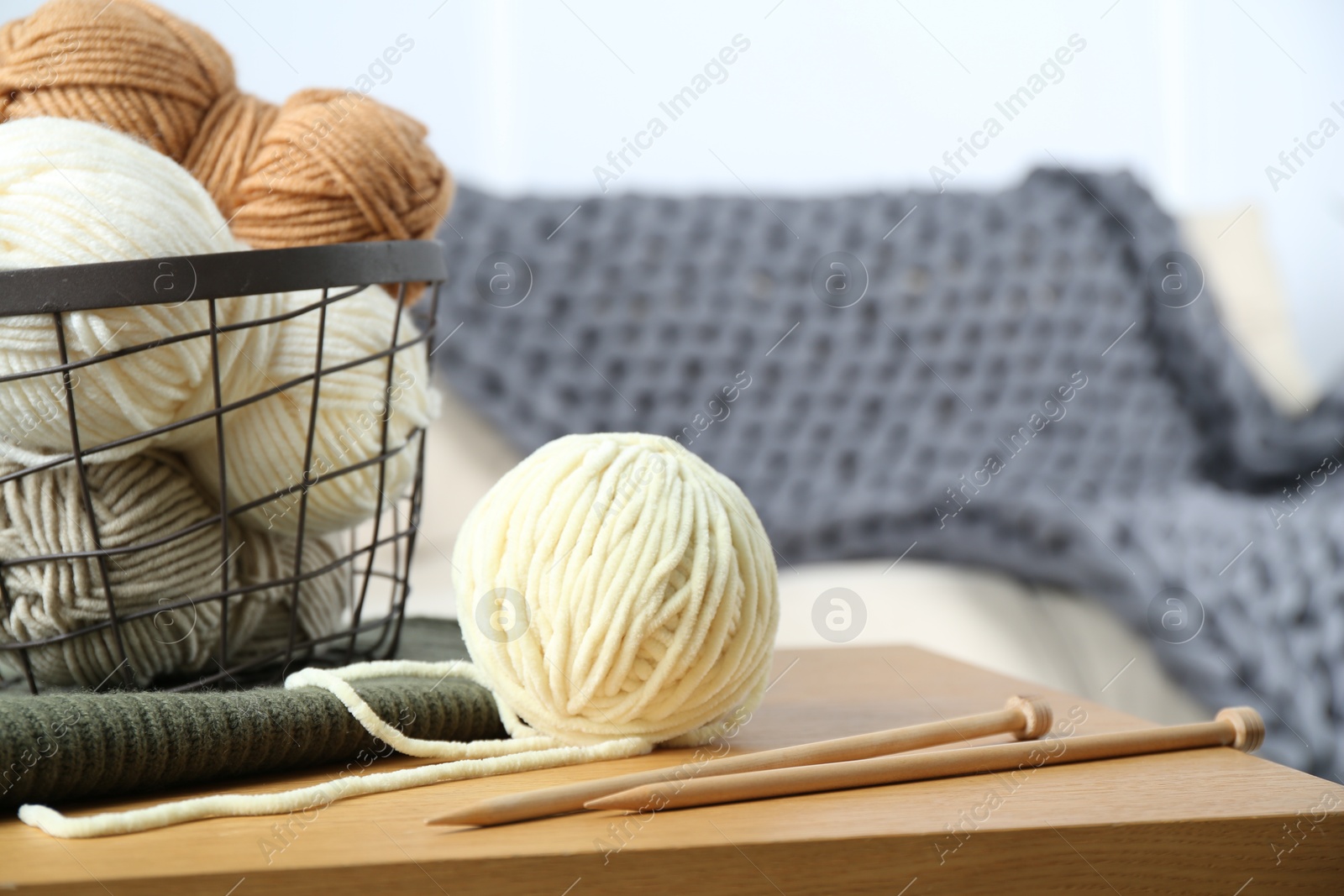 Photo of Basket with yarns, knitting needles and sweater on wooden table indoors