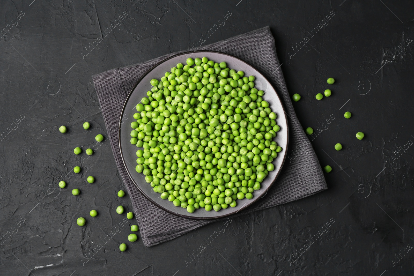 Photo of Fresh green peas in plate on black table, flat lay