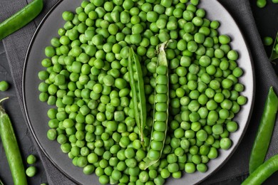 Photo of Fresh green peas and pods on black table, flat lay