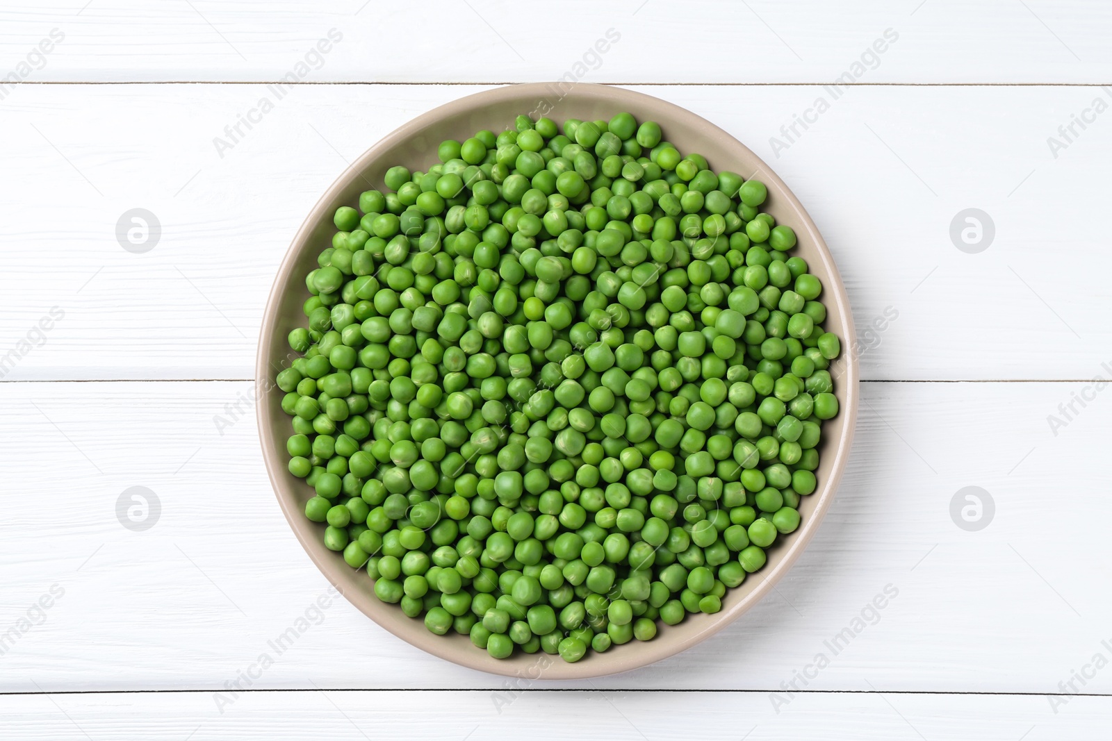 Photo of Fresh green peas in plate on white wooden table, top view