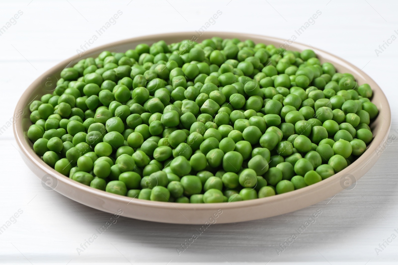 Photo of Fresh green peas in plate on white wooden table