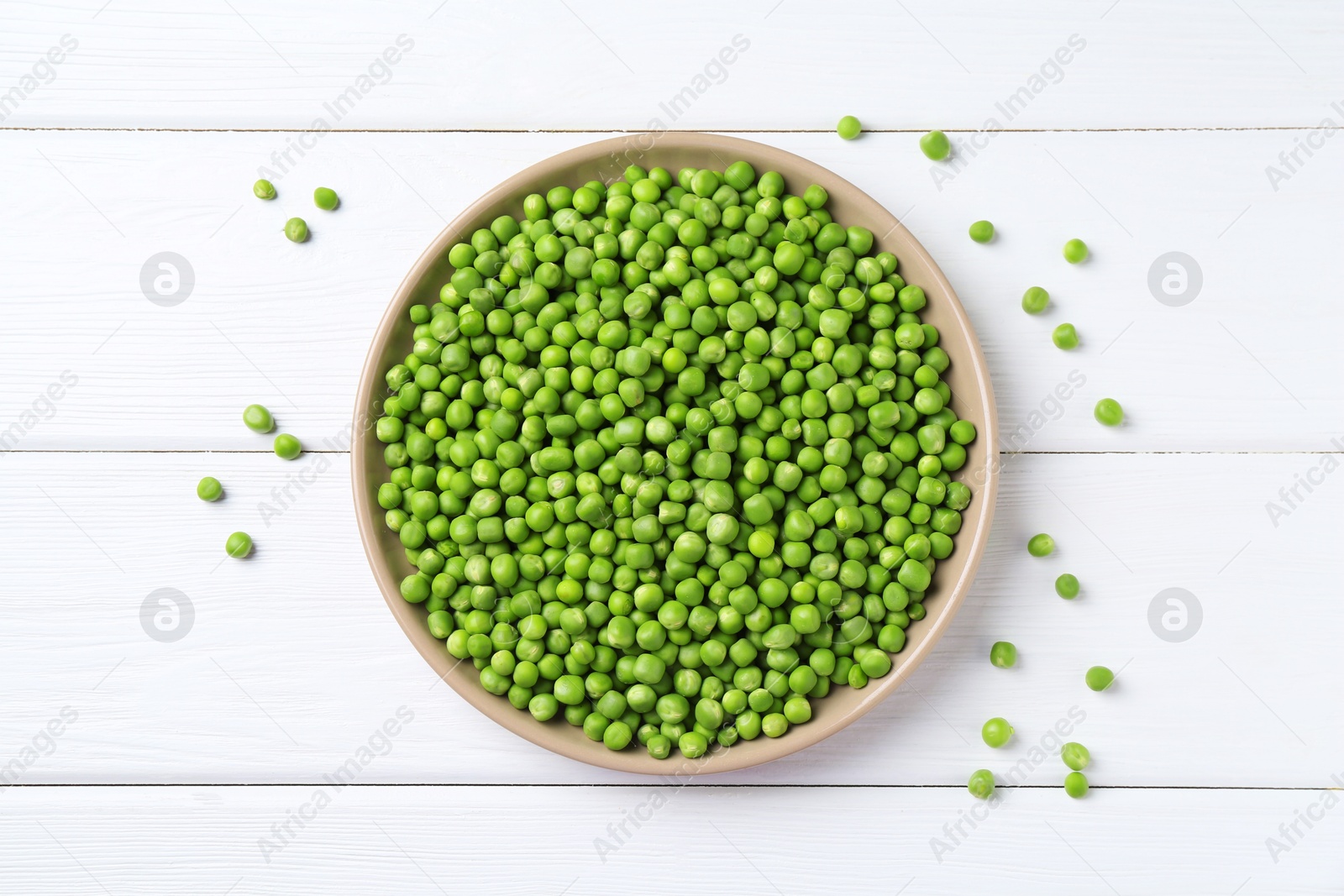 Photo of Fresh green peas in plate on white wooden table, top view