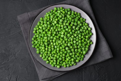 Photo of Fresh green peas in plate on black table, top view