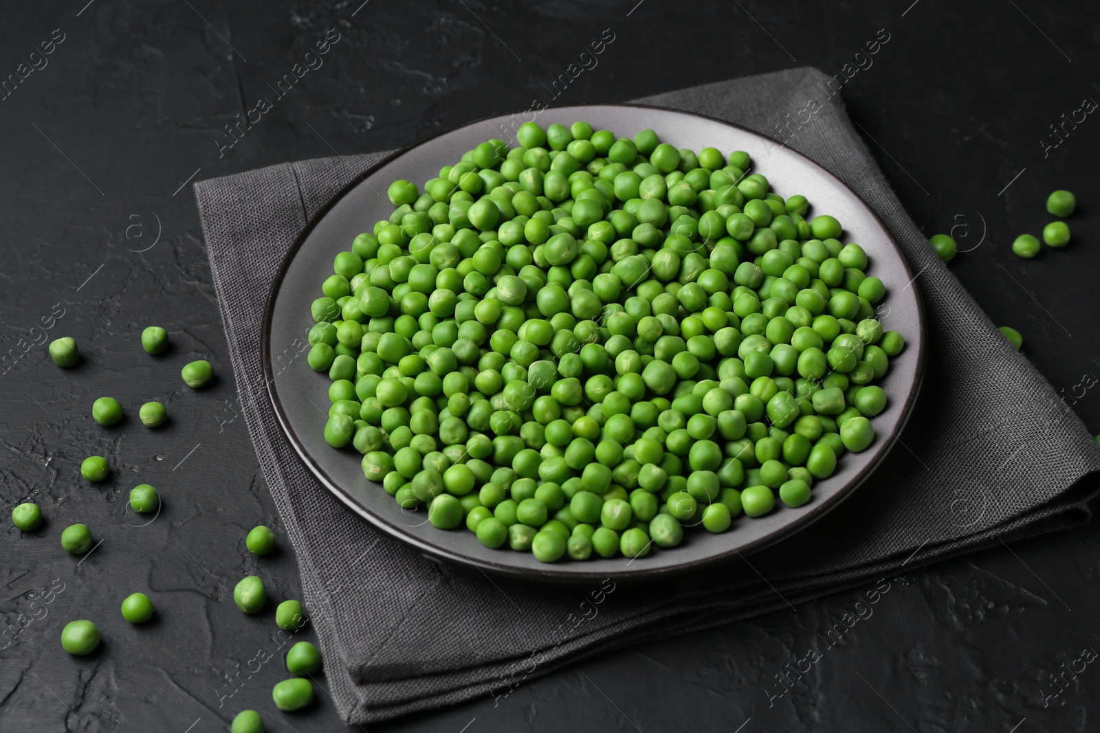 Photo of Fresh green peas in plate on black table