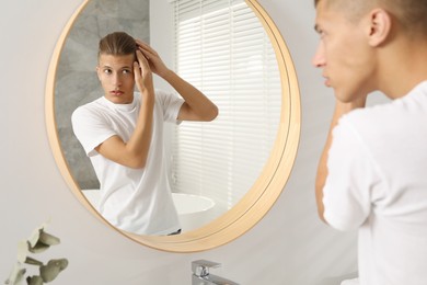 Handsome man looking at mirror in bathroom