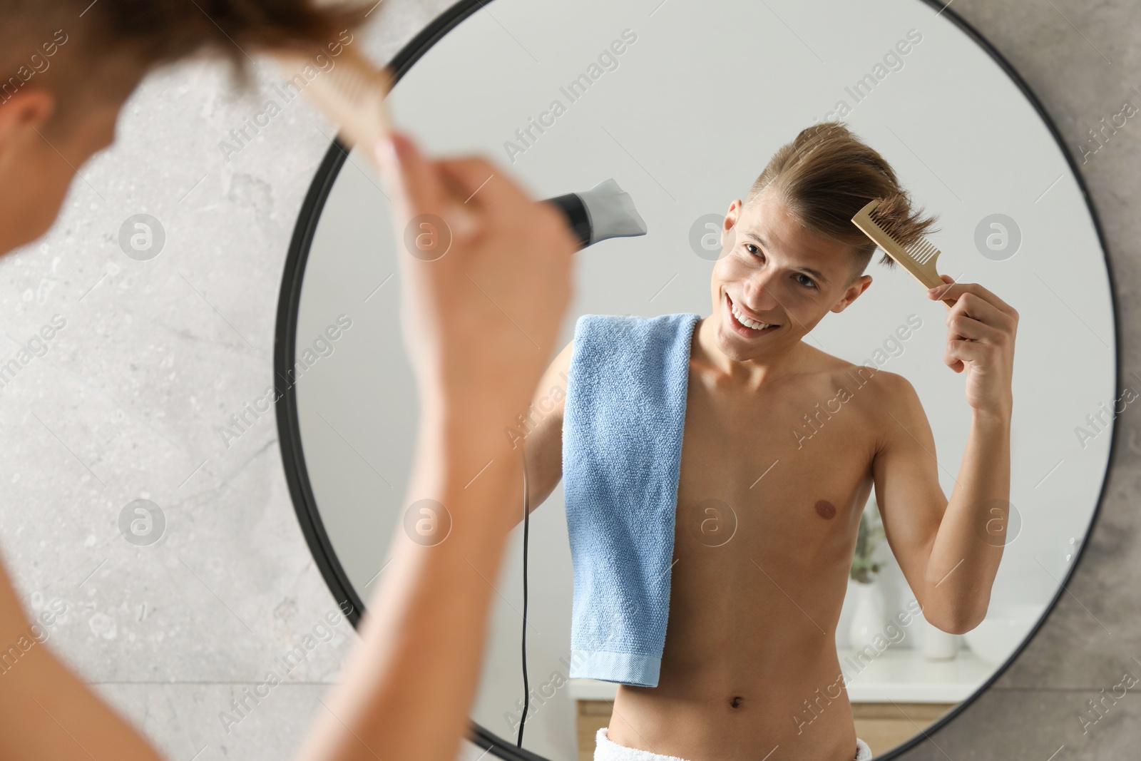 Photo of Handsome man using hair dryer near mirror in bathroom