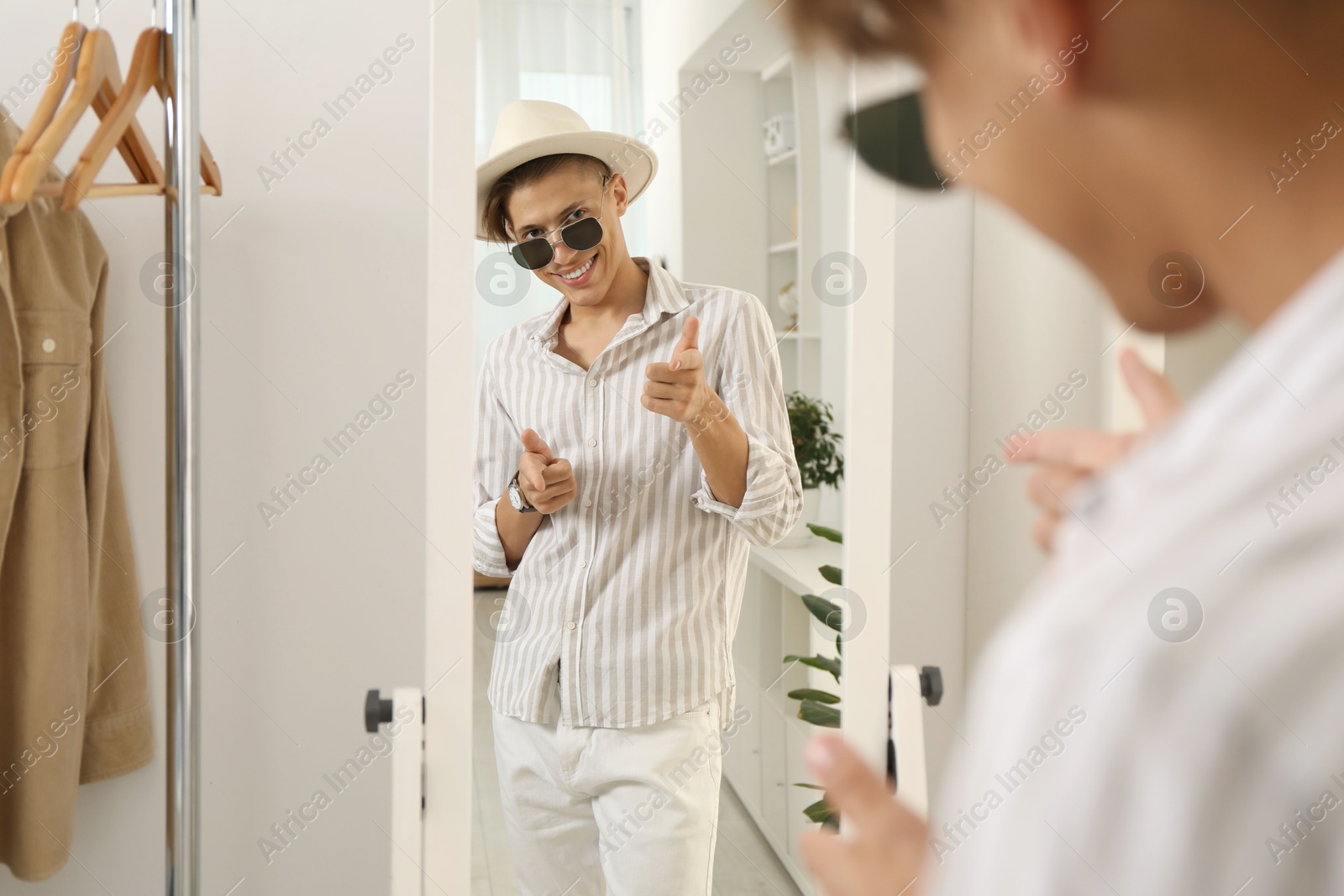 Photo of Handsome man in hat and glasses looking at mirror indoors