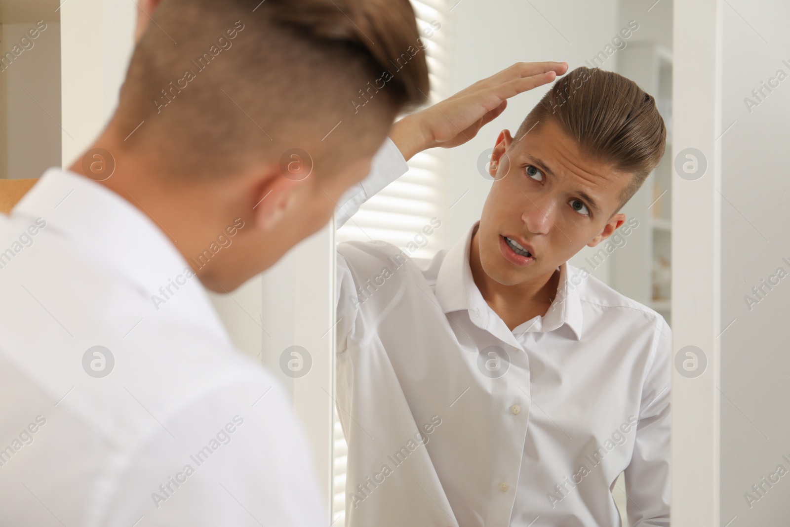 Photo of Handsome man in shirt looking at mirror indoors