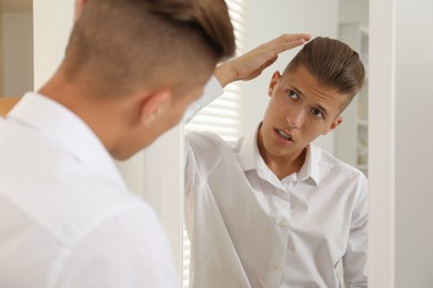 Photo of Handsome man in shirt looking at mirror indoors