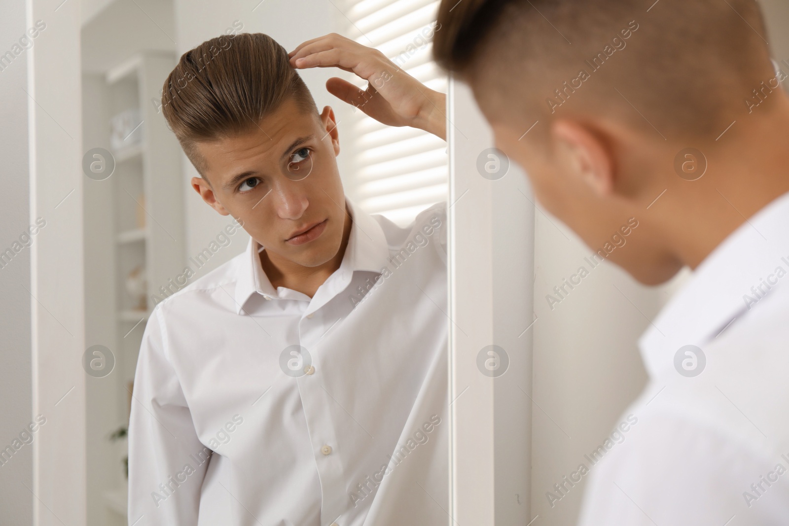 Photo of Handsome man in shirt looking at mirror indoors