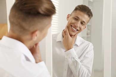 Photo of Handsome man in shirt looking at mirror indoors