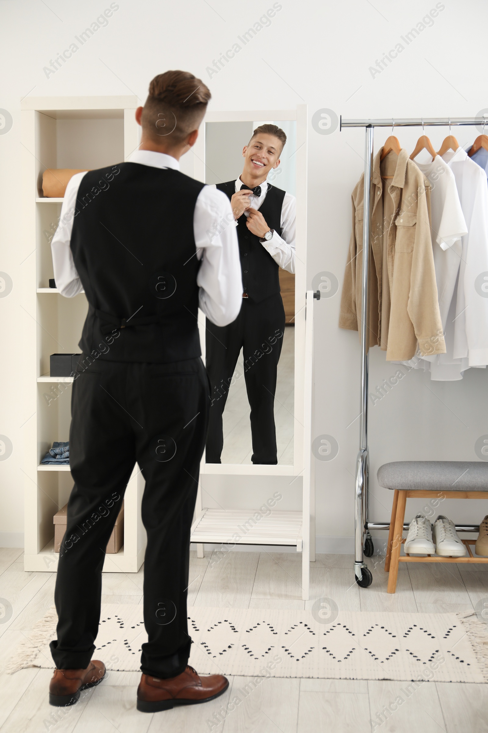 Photo of Handsome man adjusting bow tie near mirror indoors